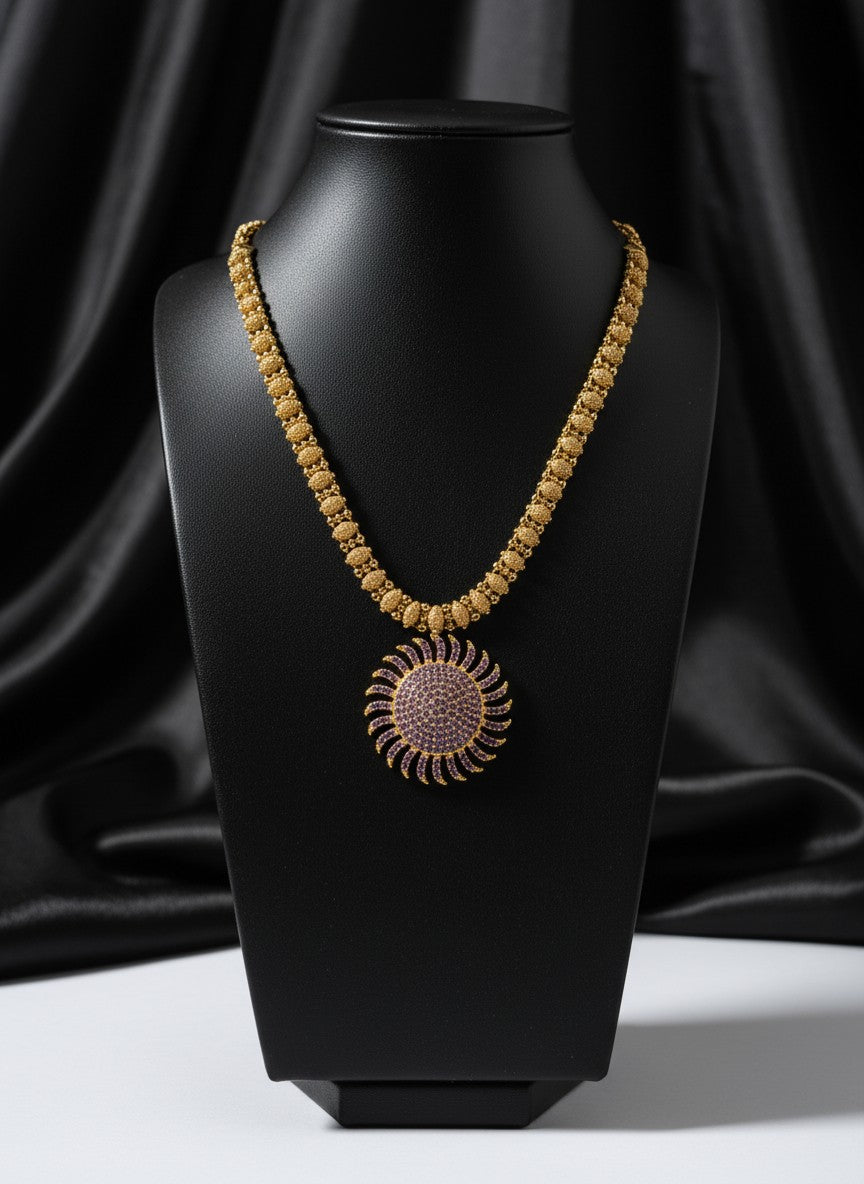 Liora By Leony gold plated necklace with a sunburst pendant adorned with small purple stones.